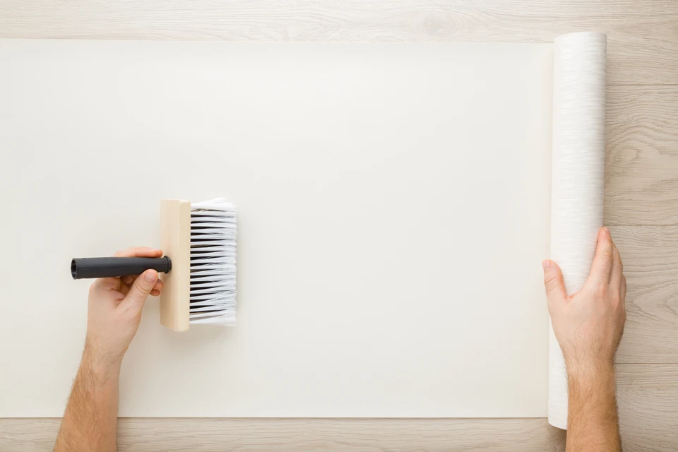 Une personne applique de la colle murale sur un mur blanc à l'aide d'un rouleau encolleur à manche noir
