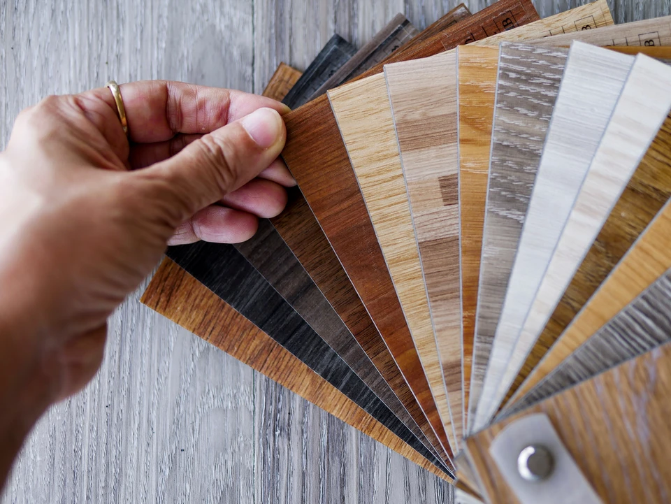 Une main tient un éventail d'échantillons de revêtements de sol stratifiés aux finitions variées